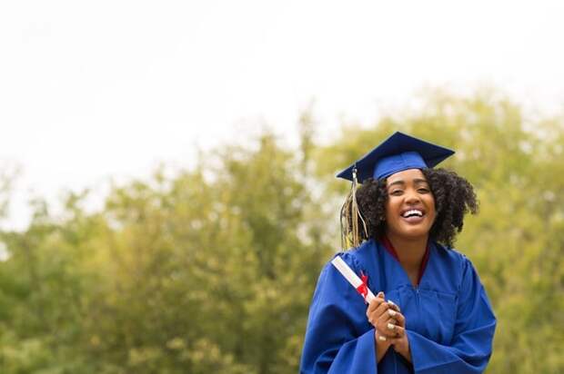 young smiling woman on graduation day wearing robe and mortarboard and holding diploma.