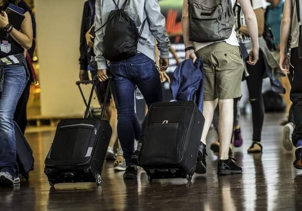 Travelers with suitcases walking through a crowded airport terminal.