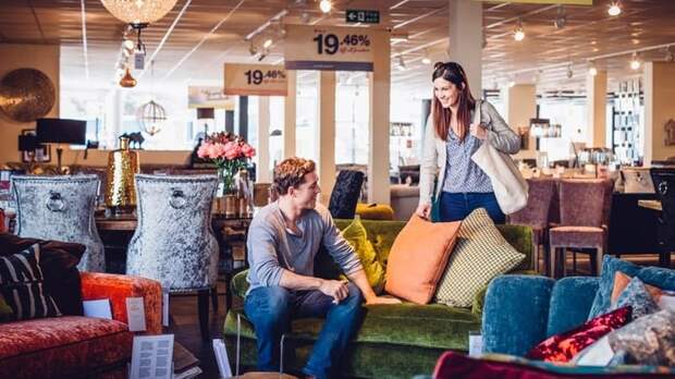 A man and woman looking at furniture in a department store with sales signs hanging from the ceiling.
