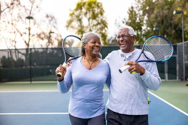 Two people hugging on a tennis court while holding racquets.