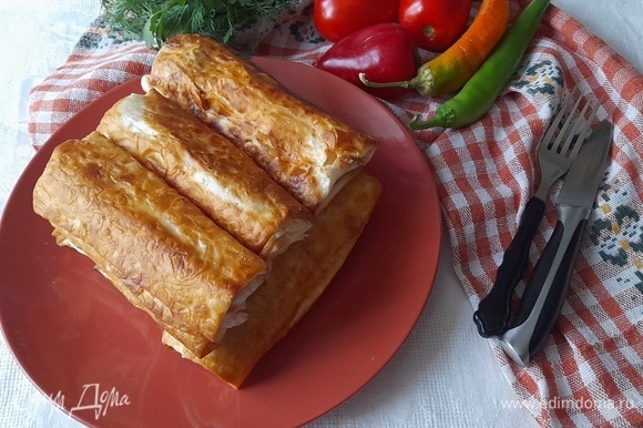 Выложить горячую закуску из лаваша с сосисками на блюдо и подать к столу со свежими овощами и зеленью.
