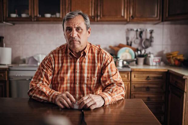 A person with a serious expression at a kitchen table.
