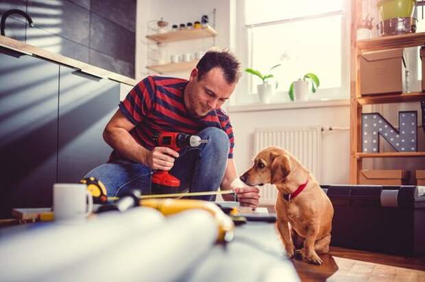 A man measuring new cabinets that he's installing in his kitchen while his dog sits next to him and watches.