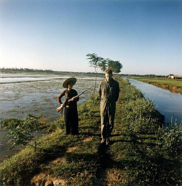 Пойманный в плен американский майор Дьюи Уодделл охраняется милиционеркой с оружием и штыком на рисовом поле. Вьетнам, 1967 .  история, люди, фото
