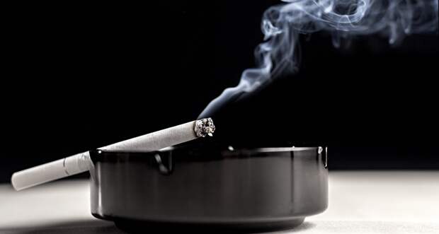a lit cigarette resting on an ashtray, smoke is rising from the cigarette