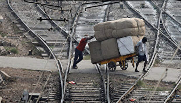 Мужчины перевозят груз через железнодорожные пути в Нью-Дели, Индия