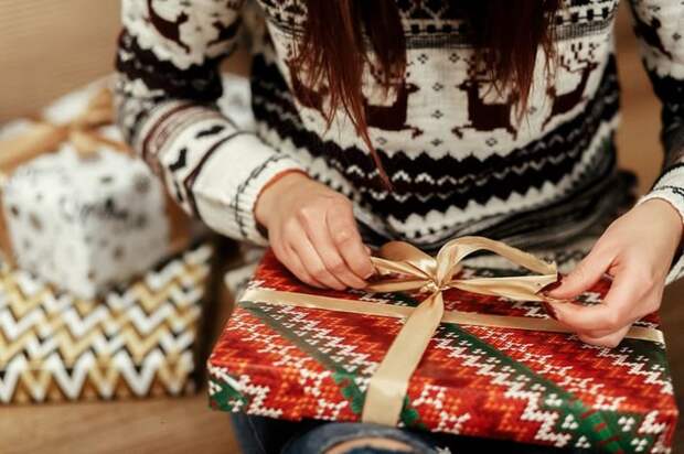 A woman in a festive sweater wrapping gifts.