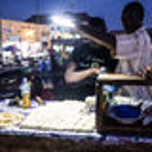 A man shines on a light so I can take a photo of his rolex stand, with fresh chapati dough ready for frying and a tray of eggs ready for cracking