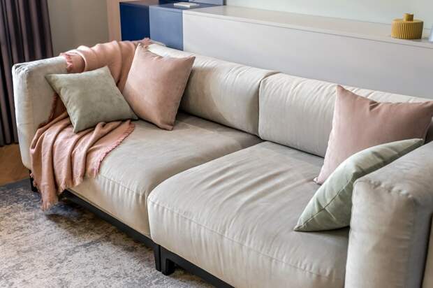 Центральное место в гостиной занял большой мягкий диван с объемными подушками в светло-серой обивке. Он не разбирается, но размеры позволяют использовать его как полноценное спальное место для одного человека.