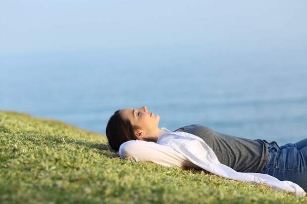 Relaxed woman lying on a grassy hill overlooking the ocean.