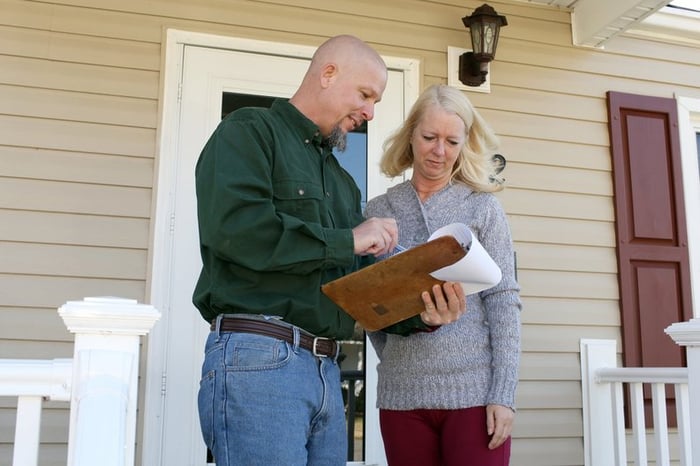 Woman on porch talking to man with clipboard.