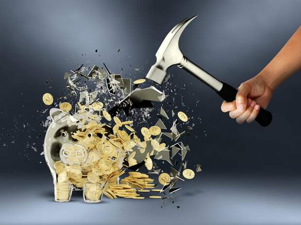 A person using a hammer to smash a glass piggy bank full of coins.
