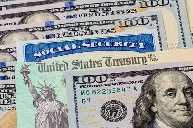 A Social Security card and a check from the U.S. Treasury in between a stack of $100 bills.