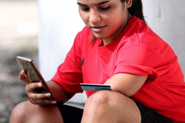 A person with an amputated left limb uses a credit card and smartphone to shop online while outside.