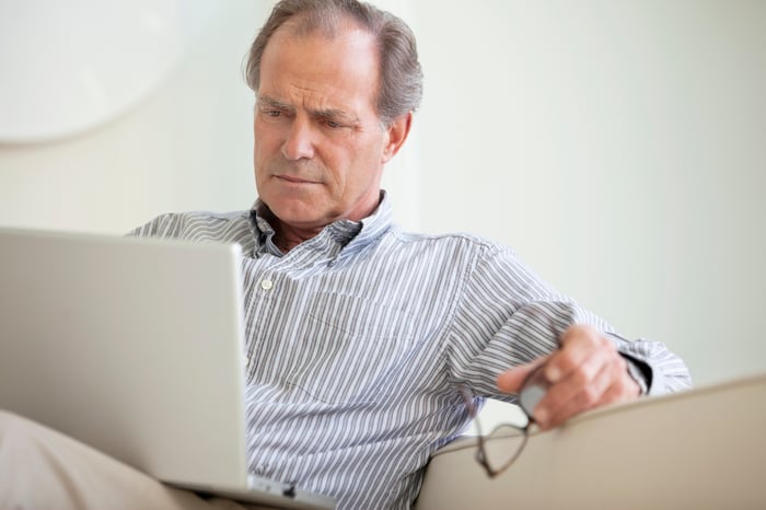 A person sitting on a couch and reading content from an open laptop on their lap.