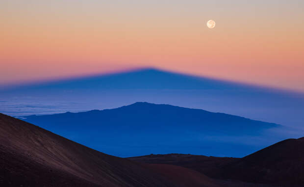 Параллельные горы Тень Мануа Кеа, самого высокого пика на Гавайях, удваивается восходящим над вулканом солнцем.