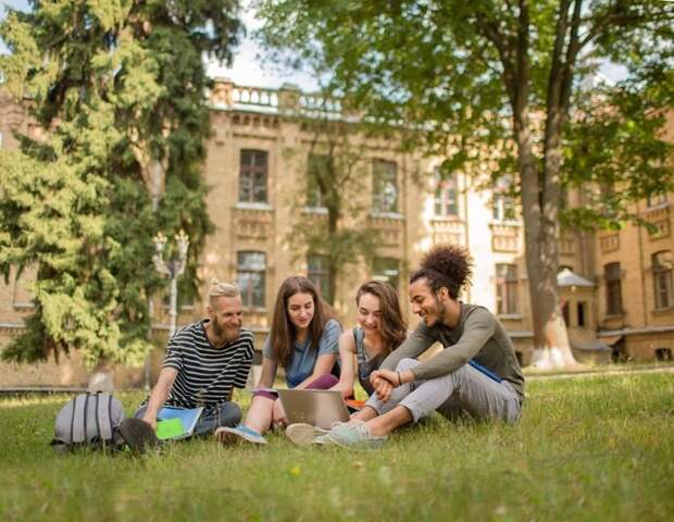 College students studying on the grass in front of a large school building.