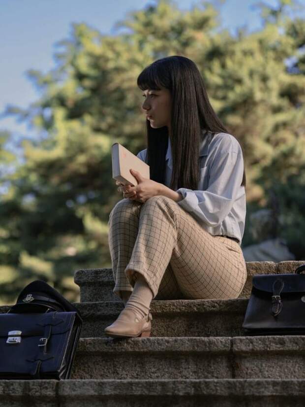 Akiko in light shirt and khaki pants sits on steps