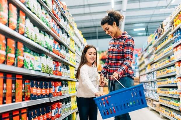 A mom and daughter walking down the aisle of a grocery and putting food in their basket.
