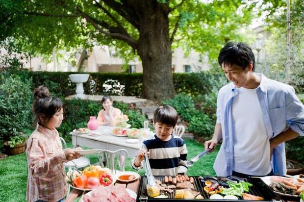 Two parents and two kids enjoying a backyard barbecue surrounded by green trees.