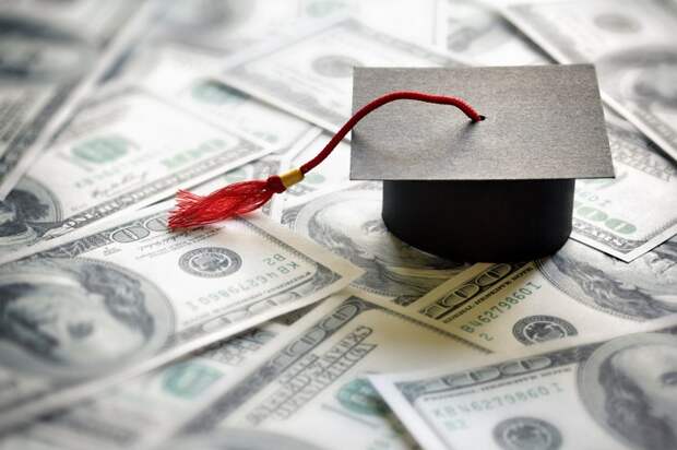 Graduation cap sitting on a pile of hundred-dollar bills