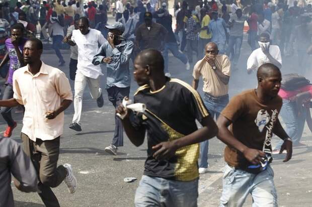 Protesters cover their mouths as they run through a cloud of tear gas during a demonstration in Senegal's capital Dakar