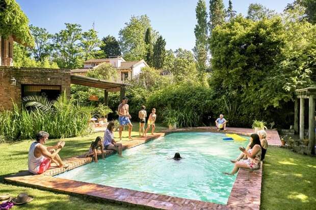 A family playing in a backyard pool surrounded by green bushes and trees.