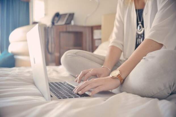 девушка сидит на кровати и печатает на ноутбуке