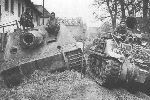 Британцы проезжают бронированной ремонтно-эвакуационной машине M4 ARV (на базе танка M4 «Шерман») мимо тяжелой немецкой САУ «Штурмтигр», брошенной экипажем из-за поломки и захваченной американцами 