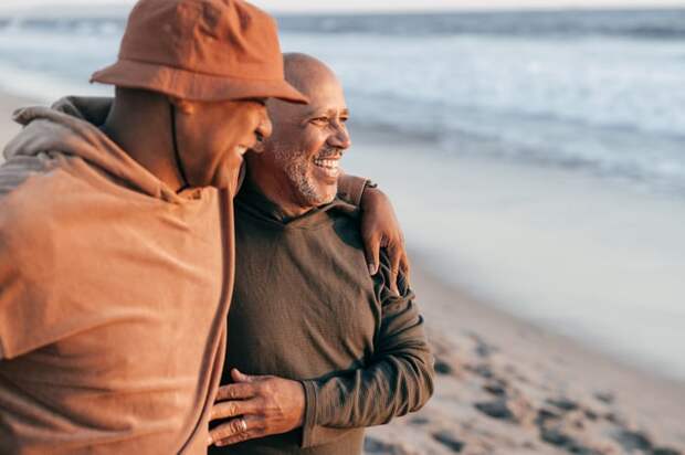 Two people standing on the beach smiling and hugging.