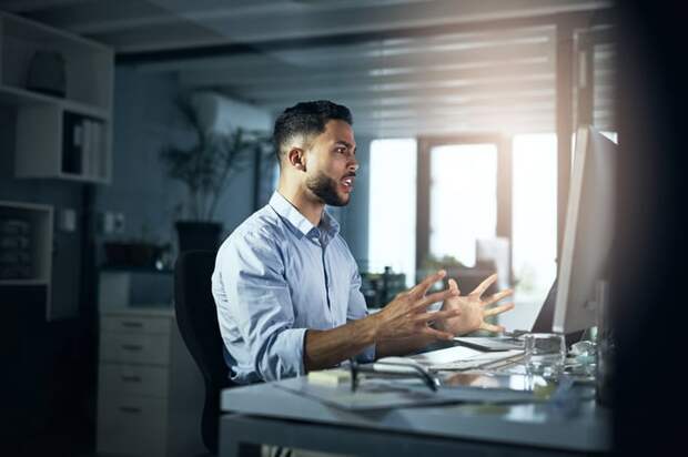 A person looks intently with hands outstretched at a computer monitor.