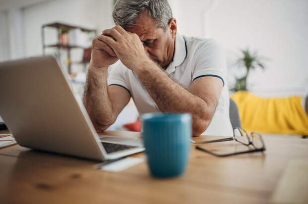 A person at a laptop holding their hands against their head.