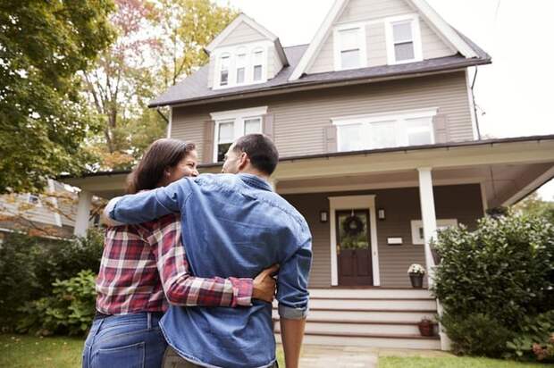 A couple with their arms around each other standing in front of their new house.