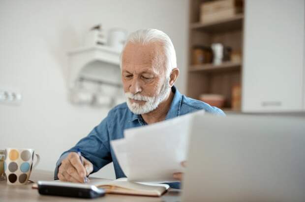A person at a table holding documents near an open laptop.