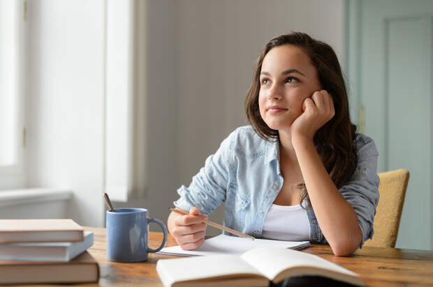 Student teenage girl studying at home daydreaming looking away