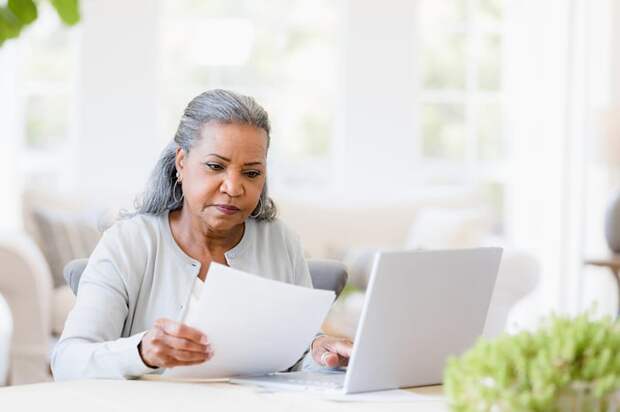 A person at a laptop is holding a document.