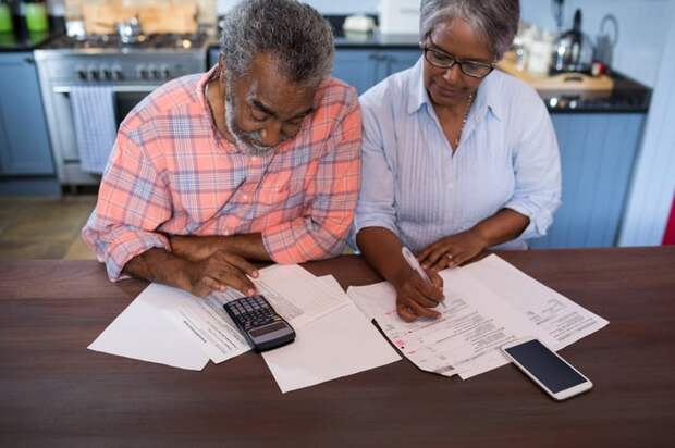 A couple in their kitchen looking at documents and a calculator.