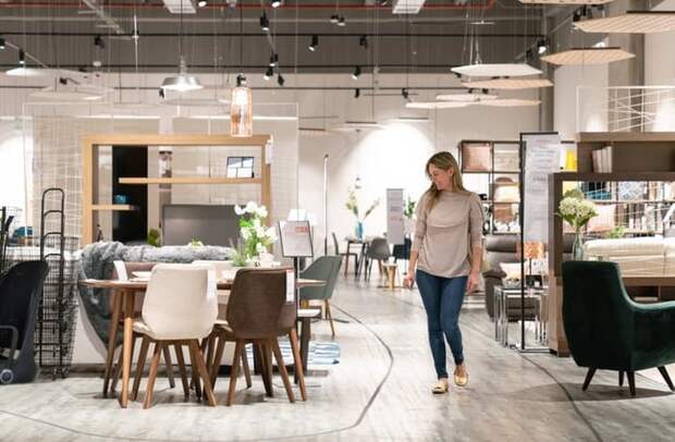 A woman walking around a furniture store and looking at a dining table set.