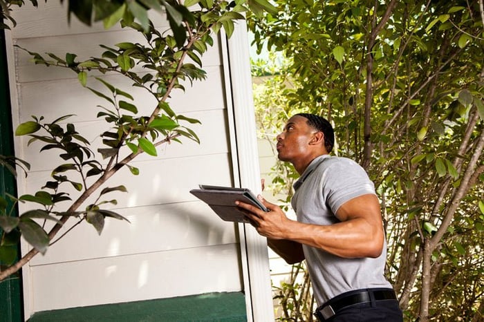 Home inspector checks the exterior walls of a house and uses a tablet to record results.