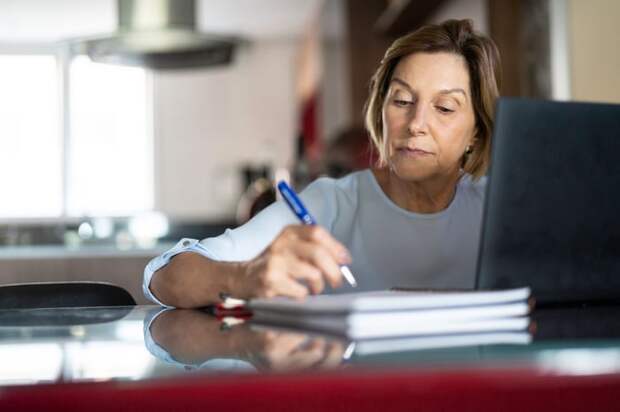 A person at a laptop holding a pen.