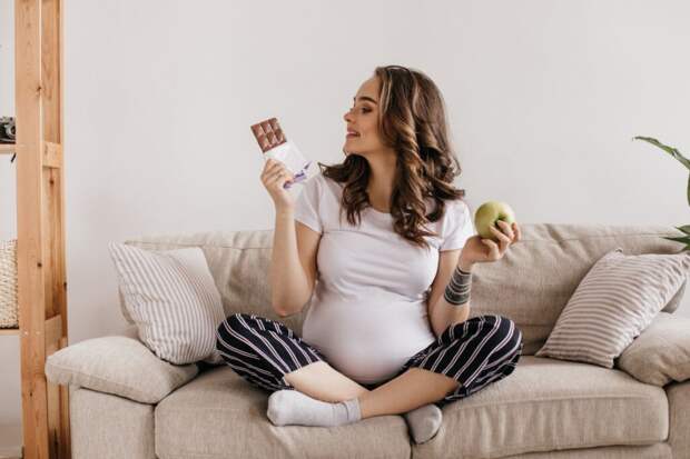 curly-brunette-pregnant-woman-looks-tasty-milk-chocolate-holds-green-apple-1024x683 Особенности питания беременных по тримстрам