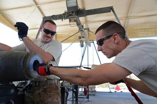 U.S. Air Force Senior Airman Christopher Reed, a munitions systems technician currently assigned to the 455th Expeditionary Maintenance Squadron, works with Senior Airman Brandon Graves, a munitions systems technician string connection wire through a bomb